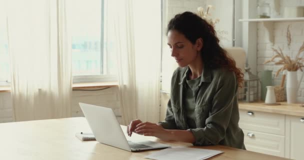 Millennial vrouw zitten aan tafel in de keuken werken op laptop — Stockvideo