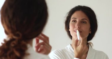 Dudak kremi sürerken aynaya bakan kadın.