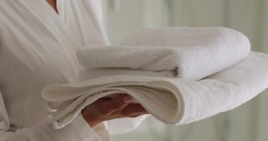 Bornozlu kadın temiz beyaz banyo havlularını tutuyor.