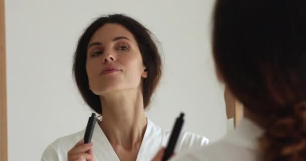 Kvinna tittar i spegeln medan du applicerar mascara på ögonfransarna — Stockvideo