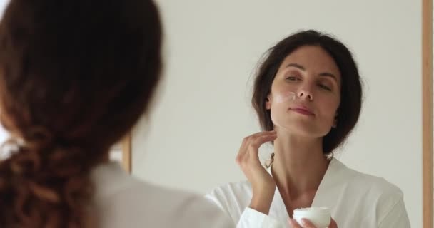 Donna riflessa nello specchio mentre si applica crema idratante per il viso — Video Stock