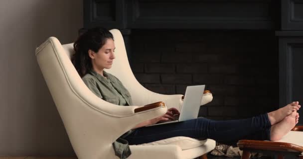 Belle femme installée dans un fauteuil en cuir reposant avec un ordinateur portable — Video