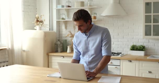 Serieuze man werkt aan laptop, schrijft gegevens, controleert documenten — Stockvideo