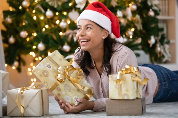 Lycklig biracial kvinna i tomte hatt ligger under julgranen — Stockfoto