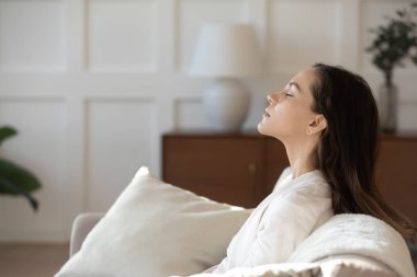 Genç kız kanepeye oturmuş, gözleri kapalı meditasyon yapıyor.