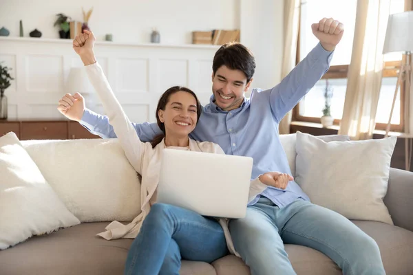 Opgewonden koppel ontvangt goed nieuws zittend op de bank met laptop — Stockfoto