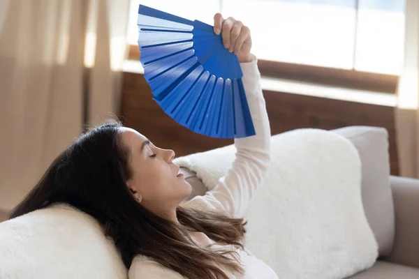 Prostrated young female fanning herself on couch suffering from heat — Stock Photo, Image