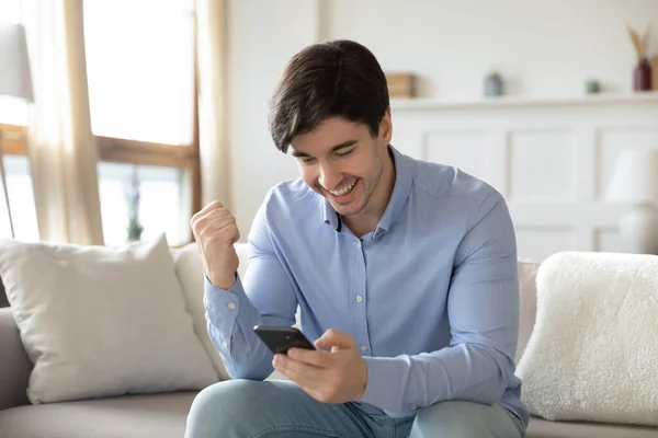 Happy millennial guy looking on cellphone screen reading good news