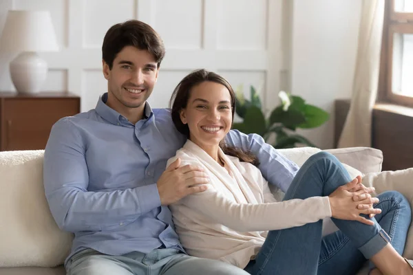 Junge Ehepartner posieren lächelnd im Wohnzimmer und schauen in die Kamera — Stockfoto