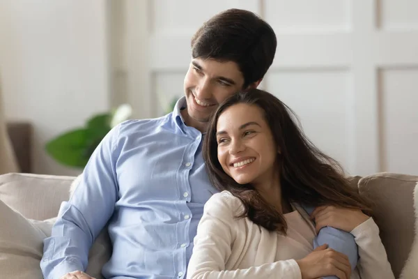 Affectionate millennial spouses sitting on couch, embracing and creating plans — Stock Photo, Image