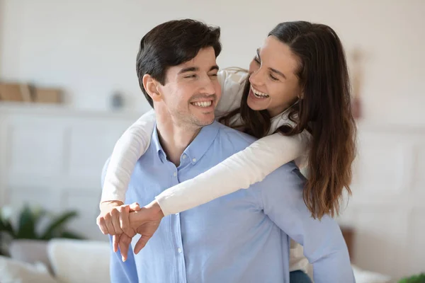 Joven riendo esposa cabalgando en marido de nuevo en sala de estar —  Fotos de Stock