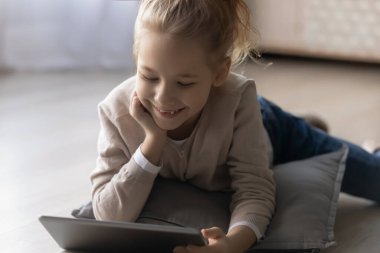 Gülümseyen küçük kız tablet kullanıyor, yerde yatıyor.