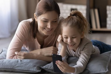 Mutlu küçük kız ve genç anne birlikte telefon kullanıyor.