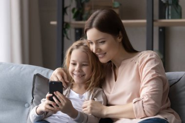 Annesiyle gülümseyen güzel kız telefon ekranına bakıyor.