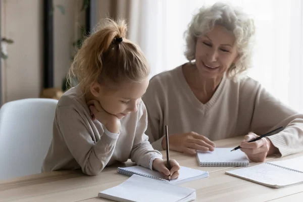 Sonriente abuela madura ayudando a su nieta con la tarea de la escuela —  Fotos de Stock