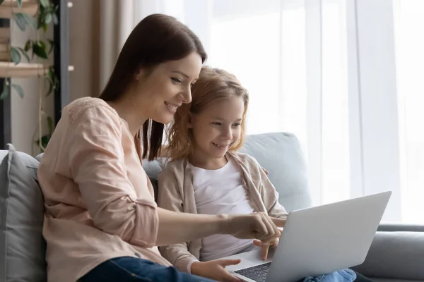 Sonriente joven madre enseñando a la pequeña hija a usar el ordenador portátil — Foto de Stock