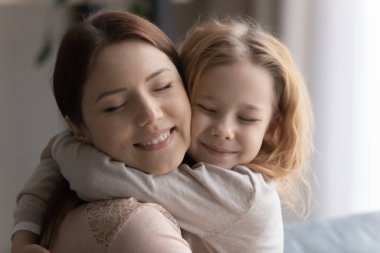 Gülümseyen, sevgi dolu bir anne, sevimli bir kıza sarılıyor.
