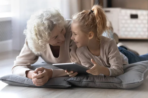 Happy mature grandmother and little girl having fun, using tablet — Stock Photo, Image