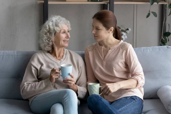 Щаслива зріла жінка з дорослою дочкою п'є чай вдома — стокове фото
