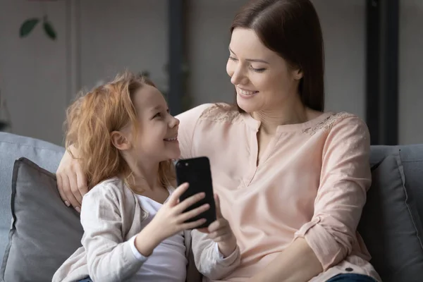 Улыбающаяся маленькая девочка и молодая мама веселятся с телефоном — стоковое фото