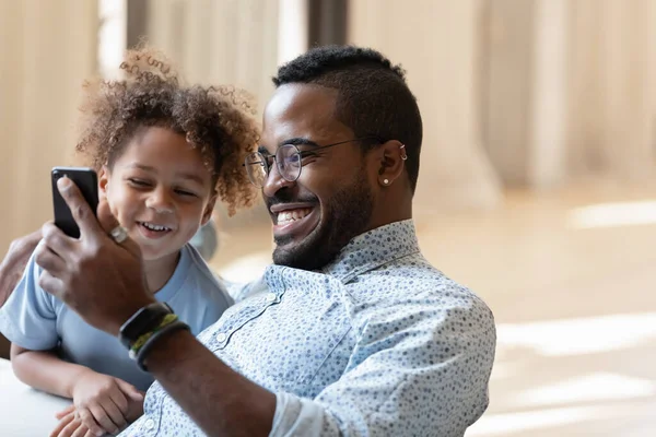 Jovem biracial papai mostrando vídeo engraçado no smartphone para filho. — Fotografia de Stock