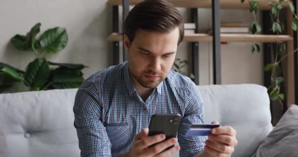 Usmívající se mladý muž zadávající informace z karty v mobilní aplikaci. — Stock video