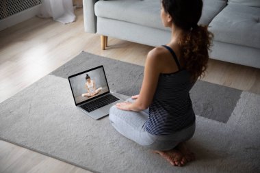 Kadın, eğitmenle webcam görüşmesinde yoga alıştırması yapıyor.