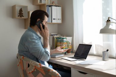 Bilgisayarda çalışan genç adam belgelerle, telefonla konuşuyor..