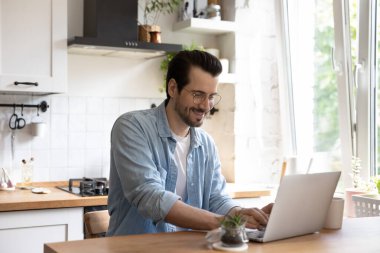 Gözlüklü mutlu genç adam uzaktan bilgisayarla çalışıyor..
