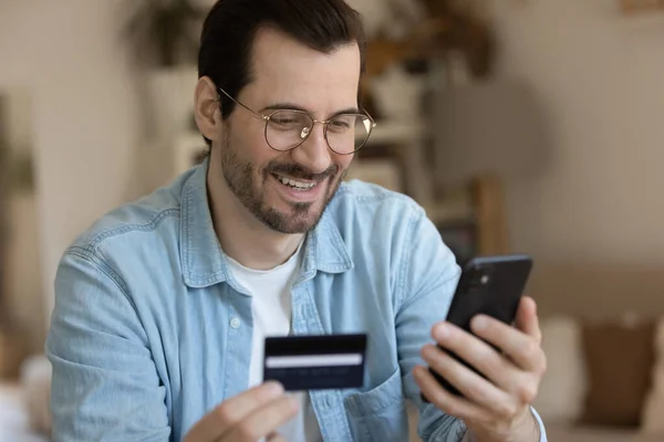 Joven hombre sonriente involucrado en compras en línea en la aplicación móvil. — Foto de Stock