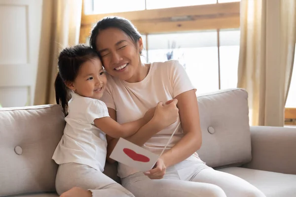 Linda niña asiática abrazando a la madre, presentando la tarjeta de felicitación —  Fotos de Stock