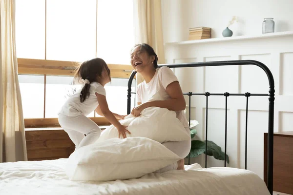 Encantada madre asiática e hija pequeña jugando a la pelea de almohadas —  Fotos de Stock