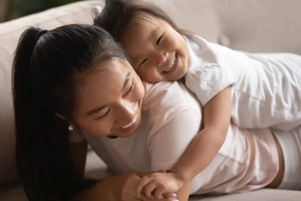 Close up adorable little daughter lying on Asian mother back — Stock Photo, Image