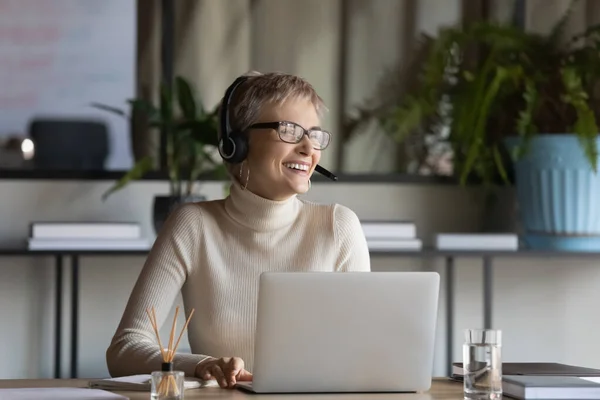 Smiling female employee in headphones laugh talking on video call — Stock Photo, Image
