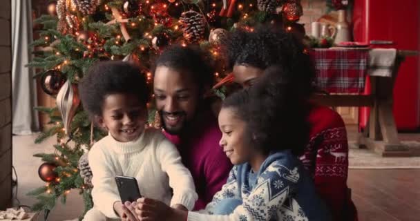 Familia africana reunida en el árbol de Navidad divirtiéndose con smartphone — Vídeo de stock