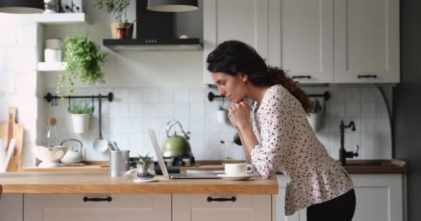Женщина, стоящая на кухне, использует ноутбук для творческой внештатной работы — стоковое видео