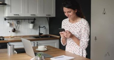 Mutfakta duran kadın akıllı telefonu tut. İnternet sohbetinin tadını çıkar.