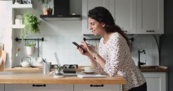 Woman standing in kitchen hold smartphone choose goods on internet — Stock Video