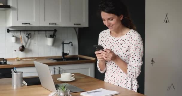 キッチンに立つ女性は楽しいオンラインチャットを楽しむスマートフォンを保持 — ストック動画