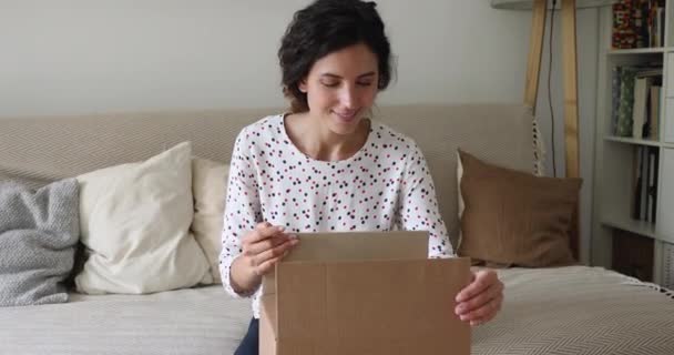 Νεαρή γυναίκα κάθεται στον καναπέ ανοίγει κουτί δεμάτων αισθάνεται ικανοποιημένος — Αρχείο Βίντεο