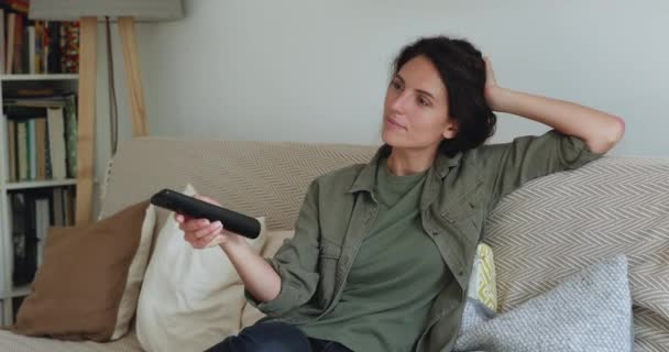 Woman relaxing on couch holds remote control switch channels — Stock Video