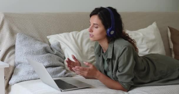 Kobieta nosi słuchawki rozmawiając przez aplikację wideokonferencyjną na laptopie — Wideo stockowe