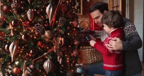 Cuidando padre su pequeño hijo cuelga bolas decorar árbol de Navidad — Vídeos de Stock