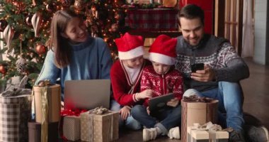 Çocuklu bir aile, süslü Noel ağacının yanında oturan aletleri kullanıyor.