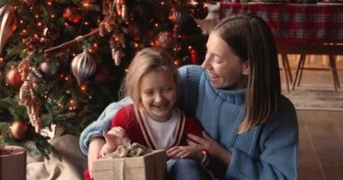 Anne, elinde hediye kutusu olan kızıyla konuş. Noel ağacının yanında otur.