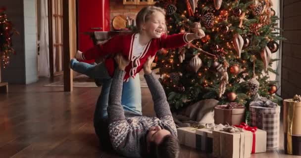Тато лежить на підлозі піднімає дочку граючи на Різдво — стокове відео