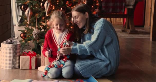 Zitten in de buurt versierde kerstboom moeder dochter maken papier slinger — Stockvideo