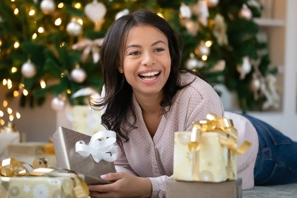 Gülümseyen melez kadın Noel ağacının altında hediyelerle yatıyor. — Stok fotoğraf