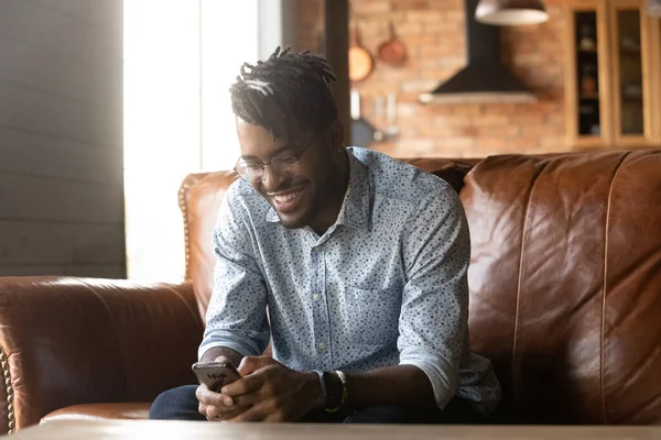 Smiling biracial man rest on couch using smartphone