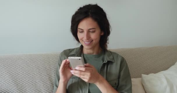 Woman sitting on couch using smartphone spend time on internet — Stock Video